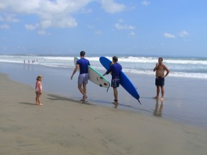 Jauh – Dua peselancar berjalan diantara seorang balita dan ayahnya di Pantai Seminyak, Kuta, Rabu (9/10/13).